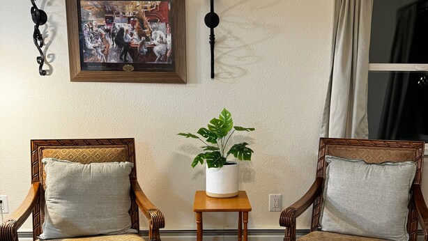 A living room with two wooden armchairs, a small table with a potted plant, a framed picture on the wall, and two wall sconces. - Cozy 2-bedroom with WiFi, Aurora viewing, central location in Fairbanks (Fairbanks)