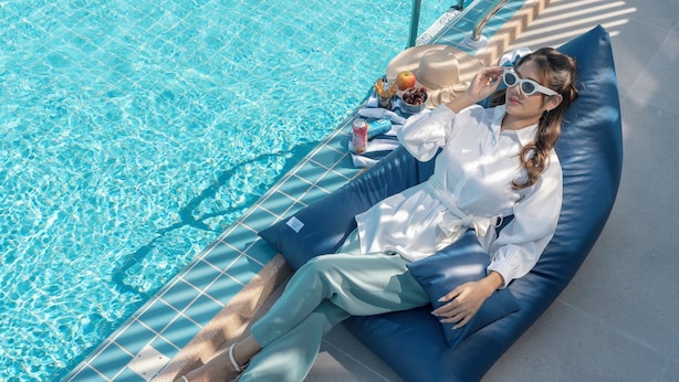 Une personne est allongée sur une chaise longue bleue au bord d’une piscine, avec la piscine en arrière-plan.