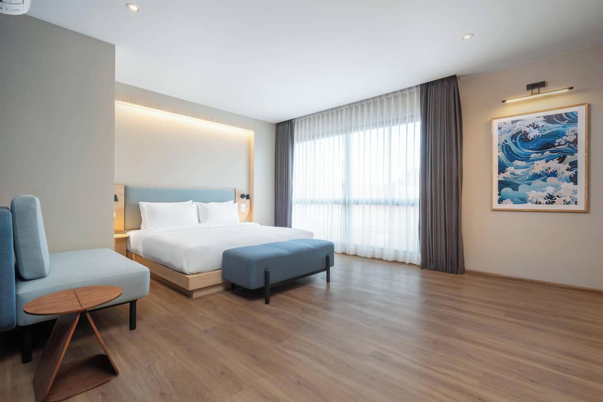 Une chambre d’hôtel moderne équipée d’un lit, d’un coin salon, d’une petite table et d’une grande fenêtre avec des rideaux.