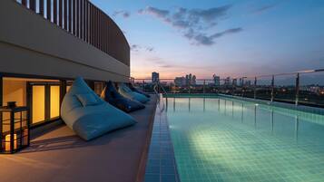 Une piscine sur le toit offrant une vue panoramique sur la ville, des chaises longues et une façade moderne.