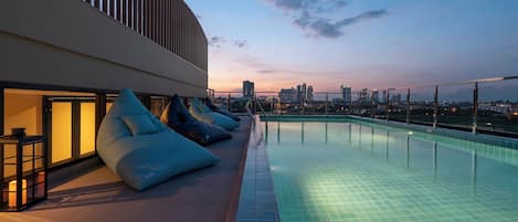 A rooftop pool with a city skyline view, lounge chairs, and a modern building facade.