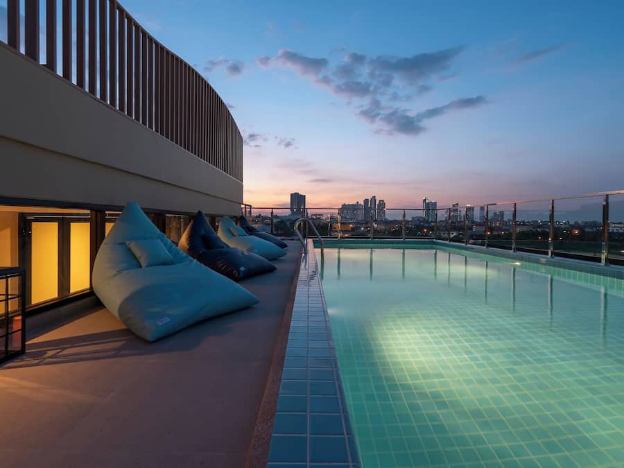 Una piscina en la azotea con vista al horizonte urbano, sillas de descanso y una fachada de edificio moderna.