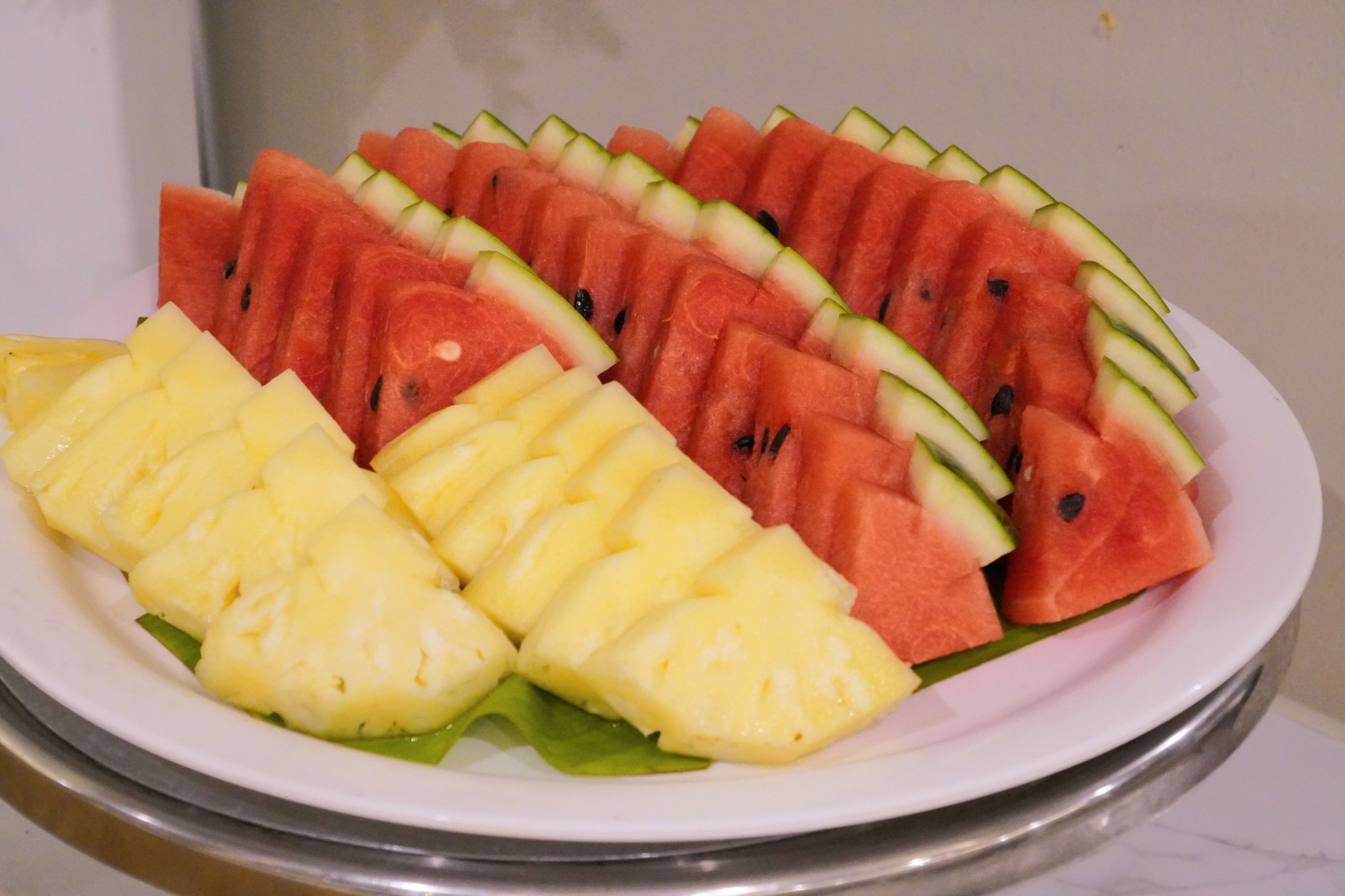 A plate with sliced watermelon and pineapple arranged on a white plate.