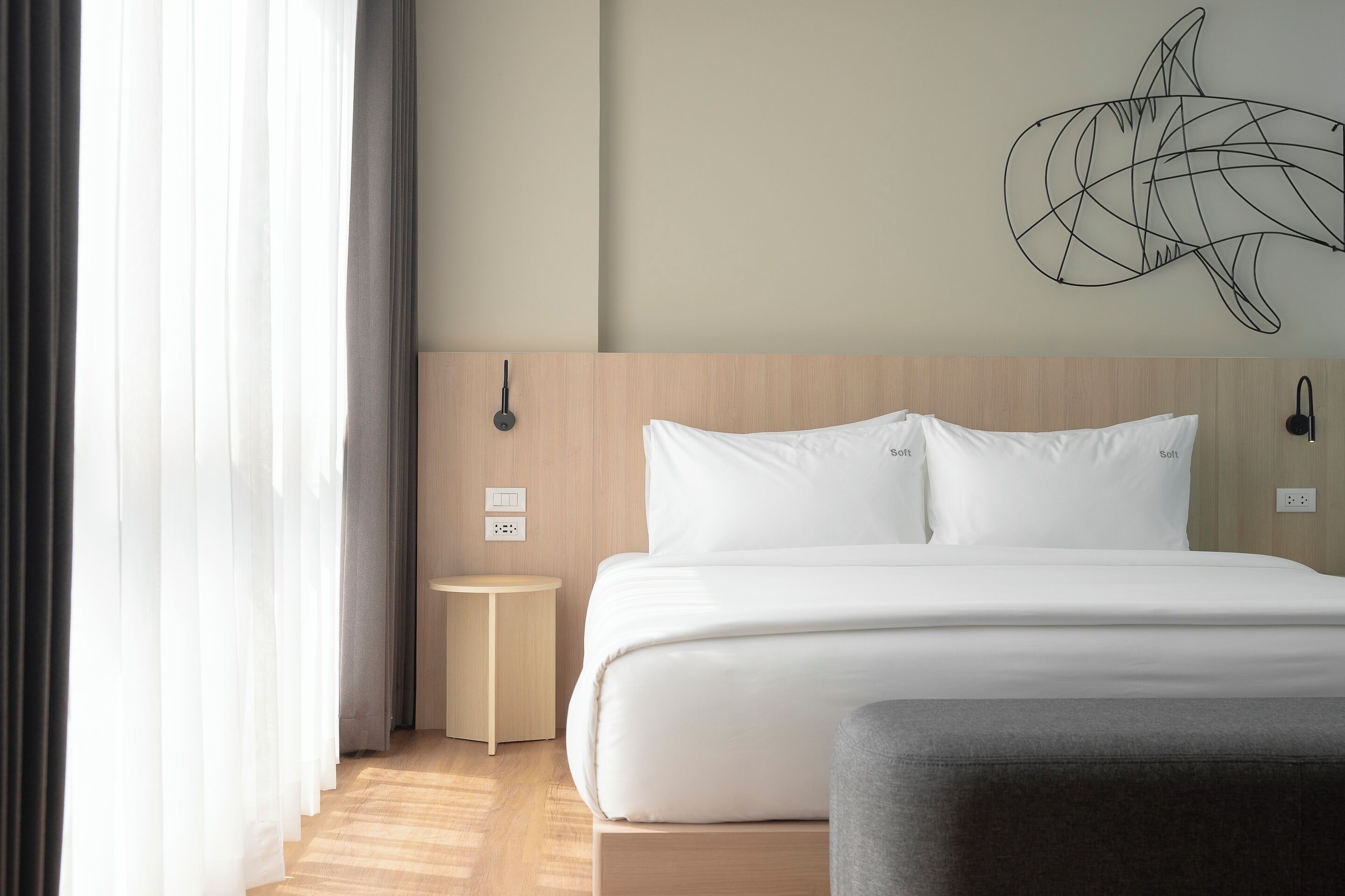 A modern hotel room with a large bed, a bedside table, and a wall-mounted artwork.