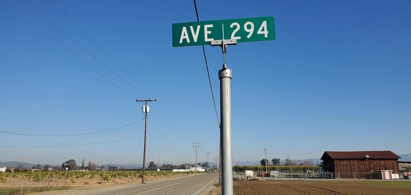 Straßenschild für AVE 294 in ländlicher Umgebung mit Weinbergen und einem Bauernhof.