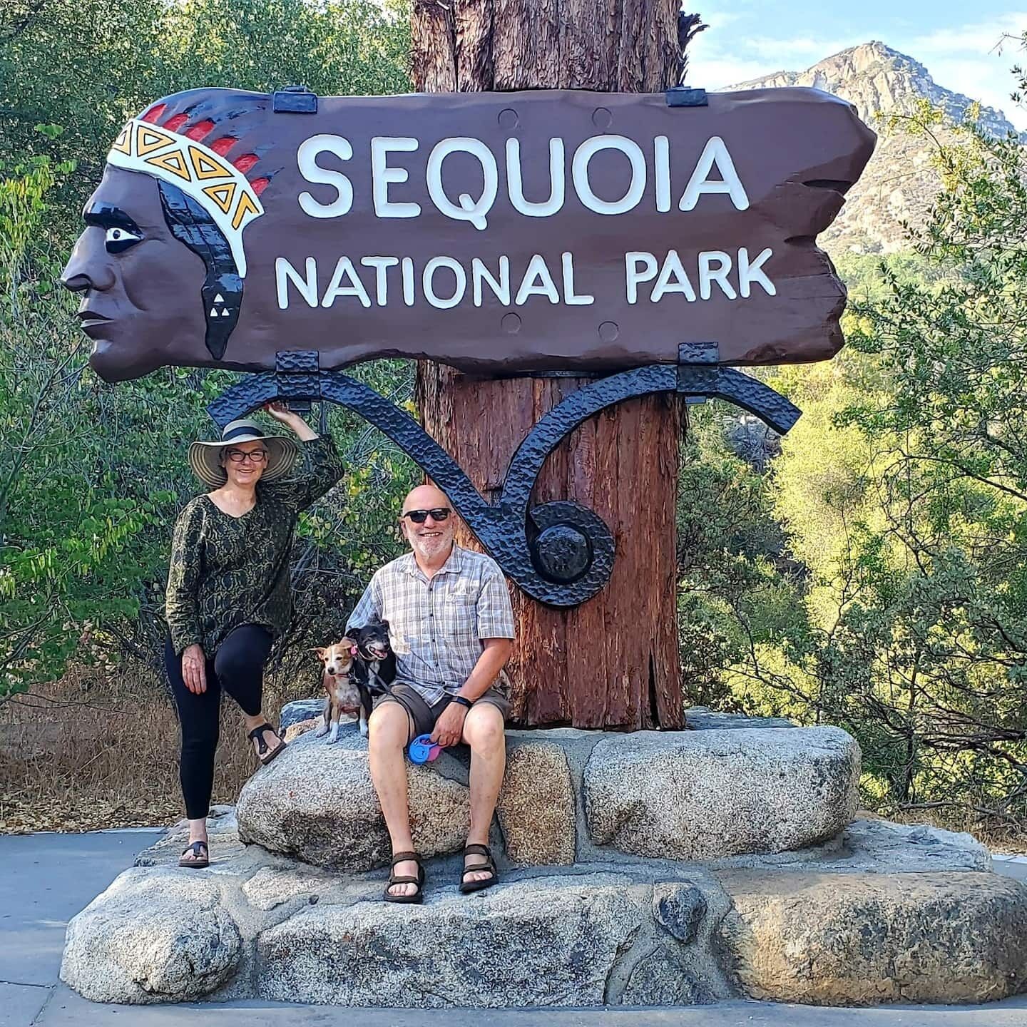 Un panneau indiquant l’entrée du parc national de Sequoia, avec un visage sculpté et un chien assis à proximité.