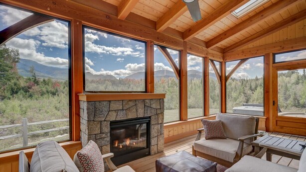 Un intérieur de chalet chaleureux avec une cheminée en pierre, de grandes fenêtres offrant une vue sur les montagnes et des sièges confortables.
