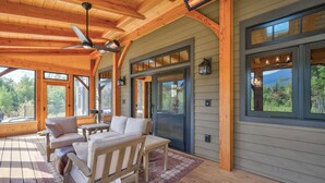 Une terrasse en bois avec un canapé et des fauteuils, de grandes fenêtres et un ventilateur de plafond.
