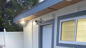 Een huis met een stenen terras, een witte deur en een raam met zonwering.