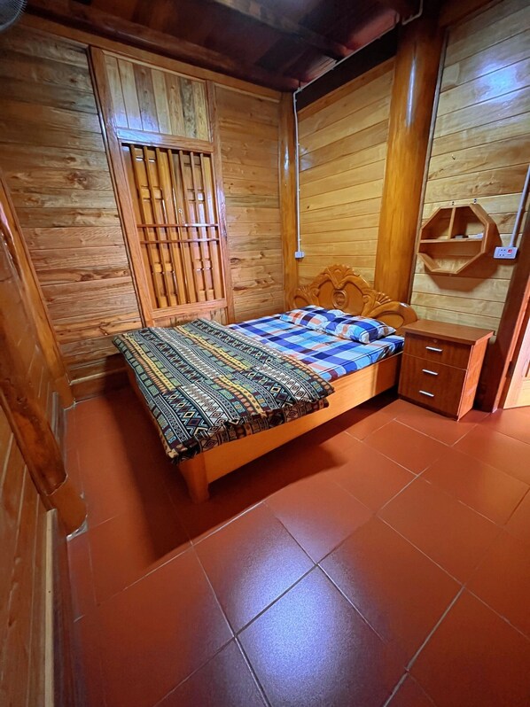 Una stanza in legno con un letto, un armadio in legno e una piccola mensola di legno.