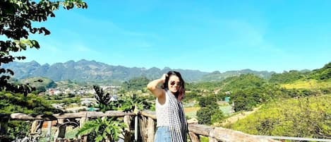 A person standing on a wooden deck with a view of a mountainous landscape.