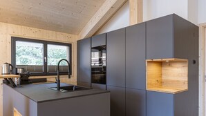 Une cuisine moderne dotée d’un îlot central, d’appareils électroménagers intégrés et d’une fenêtre donnant sur la verdure.
