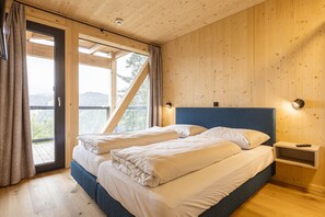 Un dormitorio de cabaña de madera con una cama, una mesita de noche y vistas a través de un ventanal amplio.