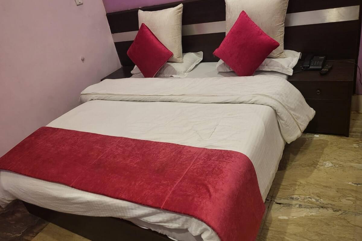 A bed with white bedding and red accents, a nightstand with a phone, and a marble floor.