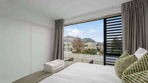 Ein Hotelzimmer mit Bett, Blick auf eine Straße und Berge, sowie ein Fenster mit Vorhängen.