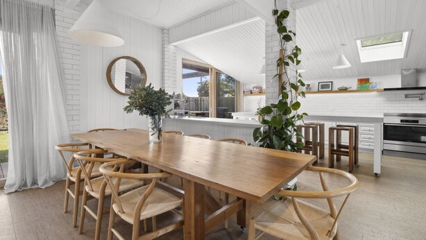 Una cocina moderna con armarios blancos, una mesa de comedor de madera y sillas de mimbre.