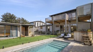 Una casa moderna con piscina, un patio cubierto y un jardín trasero cercado.