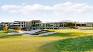 A modern building with multiple floors and large windows, surrounded by a well-maintained golf course with sand bunkers.