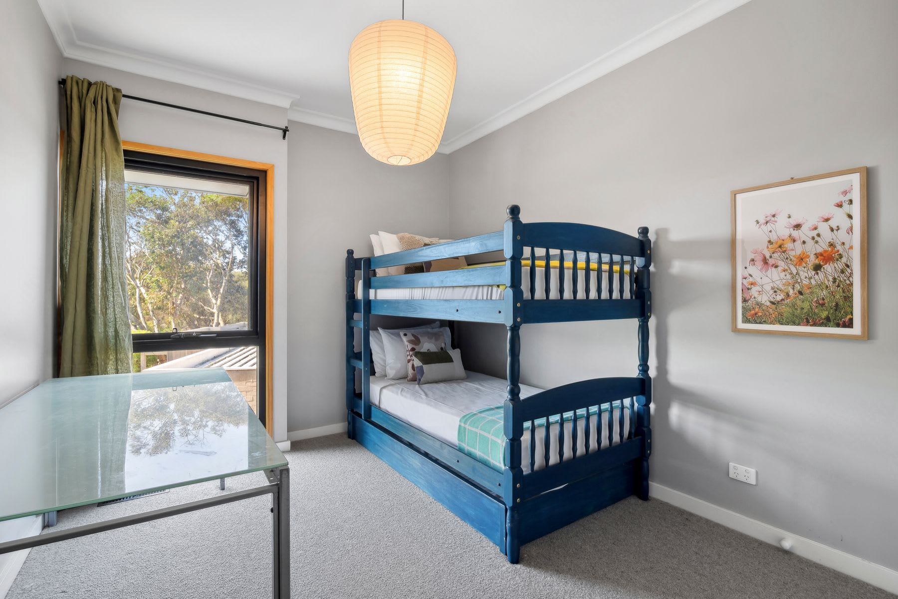A bunk bed with a glass table and a window with curtains.