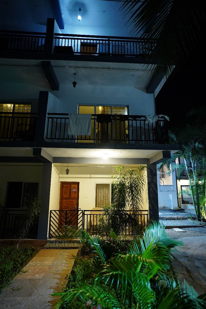 A two-story building with a balcony, a door, and a small garden area with plants.