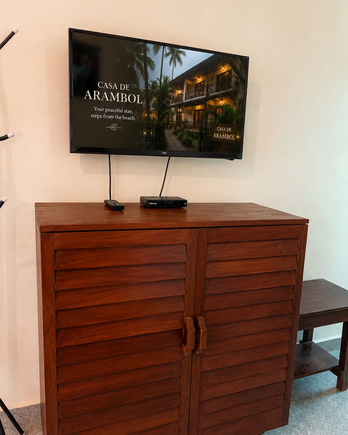 Ein Fernseher, der an einer Holzkommode befestigt ist, mit Fernbedienung und Streaming-Gerät darauf.