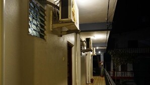Un couloir étroit et bien éclairé, doté d’un plancher en bois, de climatiseurs et d’une rambarde de balcon.