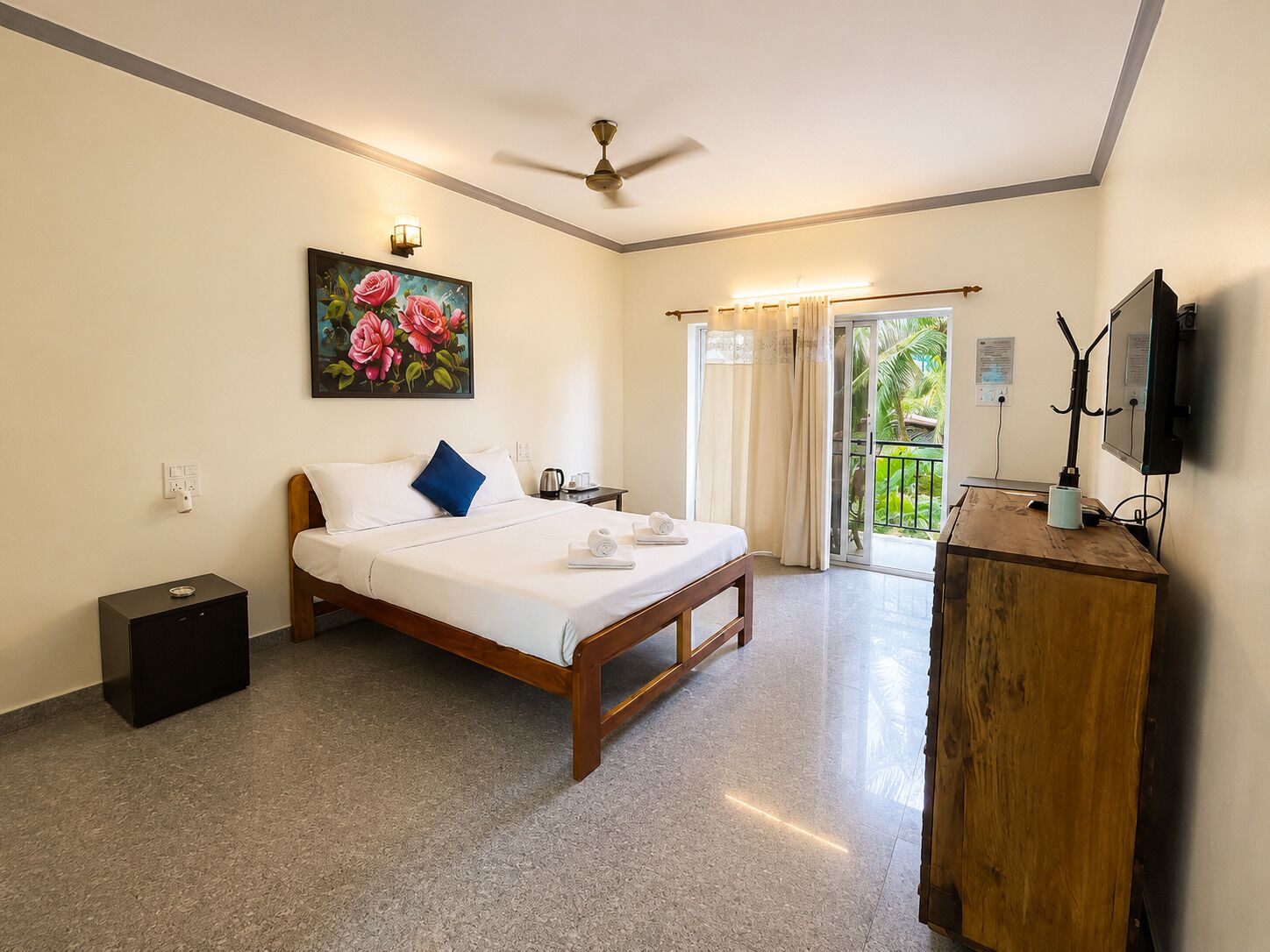 Une chambre d’hôtel avec un lit, un bureau, un ventilateur de plafond, un tableau et une vue sur l’extérieur.