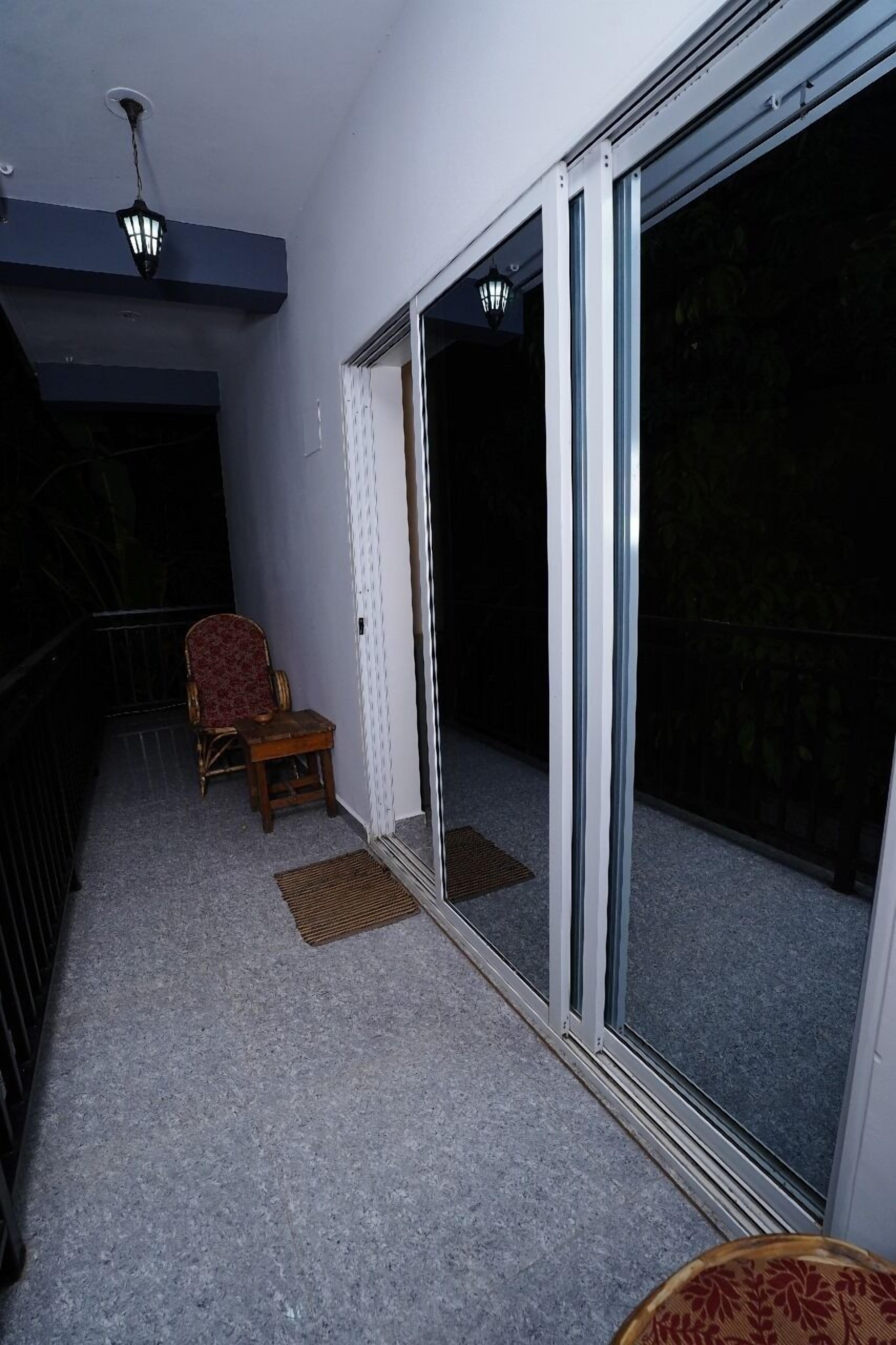 Un balcon avec une chaise et une petite table, une porte-fenêtre coulissante et un luminaire au plafond.