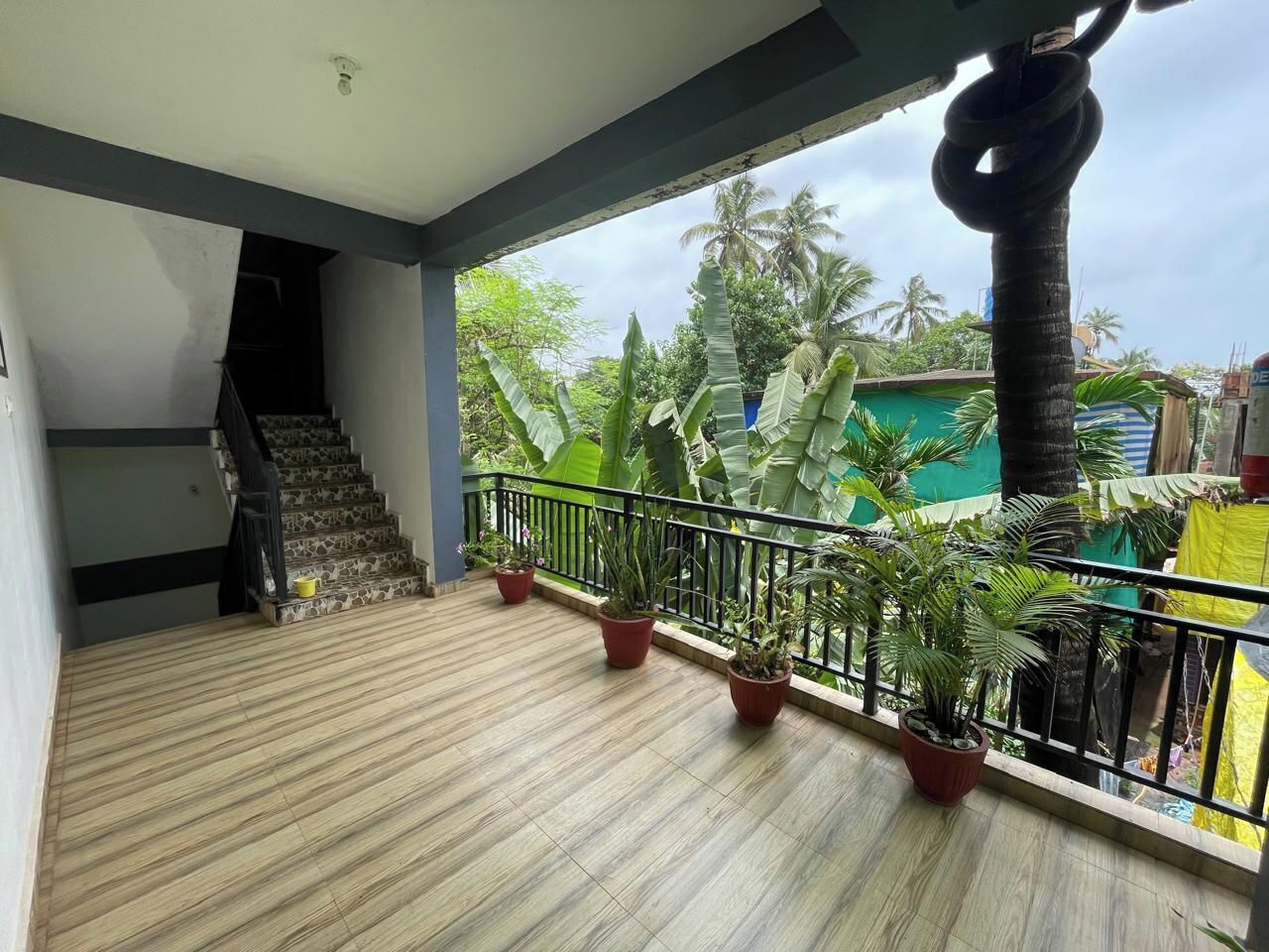 Ein Balkon mit Holzboden, Blumentöpfen und Blick auf Palmen und ein Gebäude im Hintergrund.