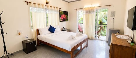 A hotel room with a bed, a desk, a television, a ceiling fan, and a balcony with curtains.