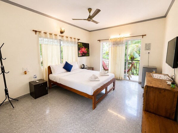 A hotel room with a bed, a desk, a television, a ceiling fan, and a balcony with curtains. - Casa De Arambol (Arambol)