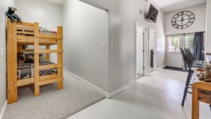 A room with a bunk bed, a clock on the wall, and a door leading to another room.