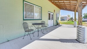 An outdoor patio with a table and chairs, a covered area with a wooden ceiling, and a building with a green exterior wall.