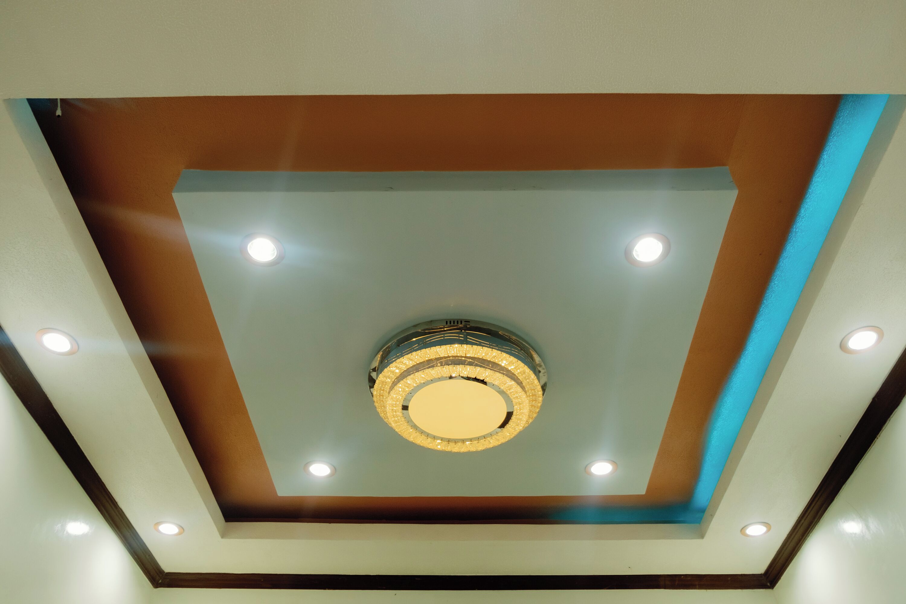 A ceiling with a central chandelier and recessed lighting.