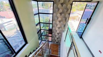 Una escalera con barandillas de vidrio, papel tapiz estampado y amplios ventanales que ofrecen vistas a edificios y zonas verdes.