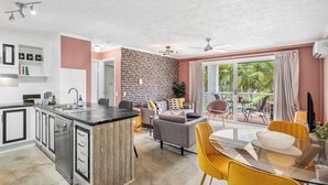 Eine moderne Küche mit Kochinsel, ein Essbereich mit gelben Stühlen und ein Balkon mit Blick auf Grünflächen.