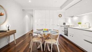 A modern kitchen with white cabinets, a round dining table with four chairs, and a wooden floor. - “MILA” Trendy Prahran 1-Bed Apartment with Balcony (Prahran)