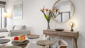 A modern living room with a glass dining table, a sofa, a console table with a vase of flowers, a mirror, and a framed map on the wall. - “MILA” Trendy Prahran 1-Bed Apartment with Balcony (Prahran)