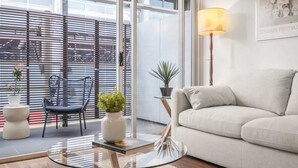 A modern living room with a glass coffee table, a sofa, a chair, and potted plants. - “MILA” Trendy Prahran 1-Bed Apartment with Balcony (Prahran)