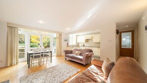 A spacious living room with a sofa, a dining table with chairs, and a kitchen area visible through an open door. - The Stables Cottage Aboyne Royal Deeside (Aboyne)