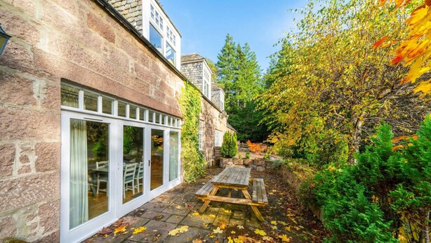 A stone building with large glass doors and a wooden bench in a garden with autumn leaves. - The Stables Cottage Aboyne Royal Deeside (Aboyne)