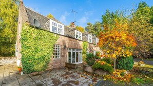 A traditional stone house with ivy-covered walls, a tiled patio, and a tree with autumn leaves. - The Stables Cottage Aboyne Royal Deeside (Aboyne)