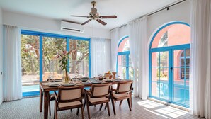 A dining area with a table set for four, a ceiling fan, and large windows with blue frames. - Casa Amore Baia (Mandrem)