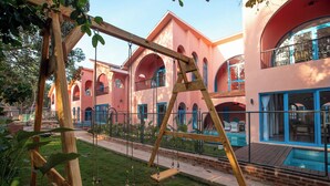A playground with swings and a fenced area, surrounded by a building with arched windows and a pool. - Casa Amore Baia (Mandrem)