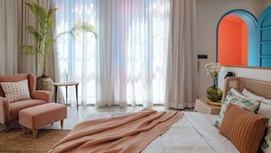 A bedroom with a bed, a chair, a small table, a potted plant, and a vase with flowers. - Casa Amore Baia (Mandrem)