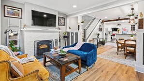A living room with a fireplace, a sofa, a coffee table, and a dining area with chairs and a table. - Sophia's Garden Cottage-  Quality & Stylish & Car-Ps & Walk-Zone & Kid Friendly  (Ardmore)