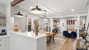 A modern kitchen with white cabinetry, a central island, pendant lighting, and a dining area with a blue sofa and wooden table. - Sophia's Garden Cottage-  Quality & Stylish & Car-Ps & Walk-Zone & Kid Friendly  (Ardmore)