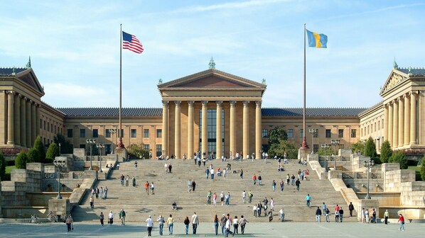 A grand building with a central staircase, large columns, and two flags.