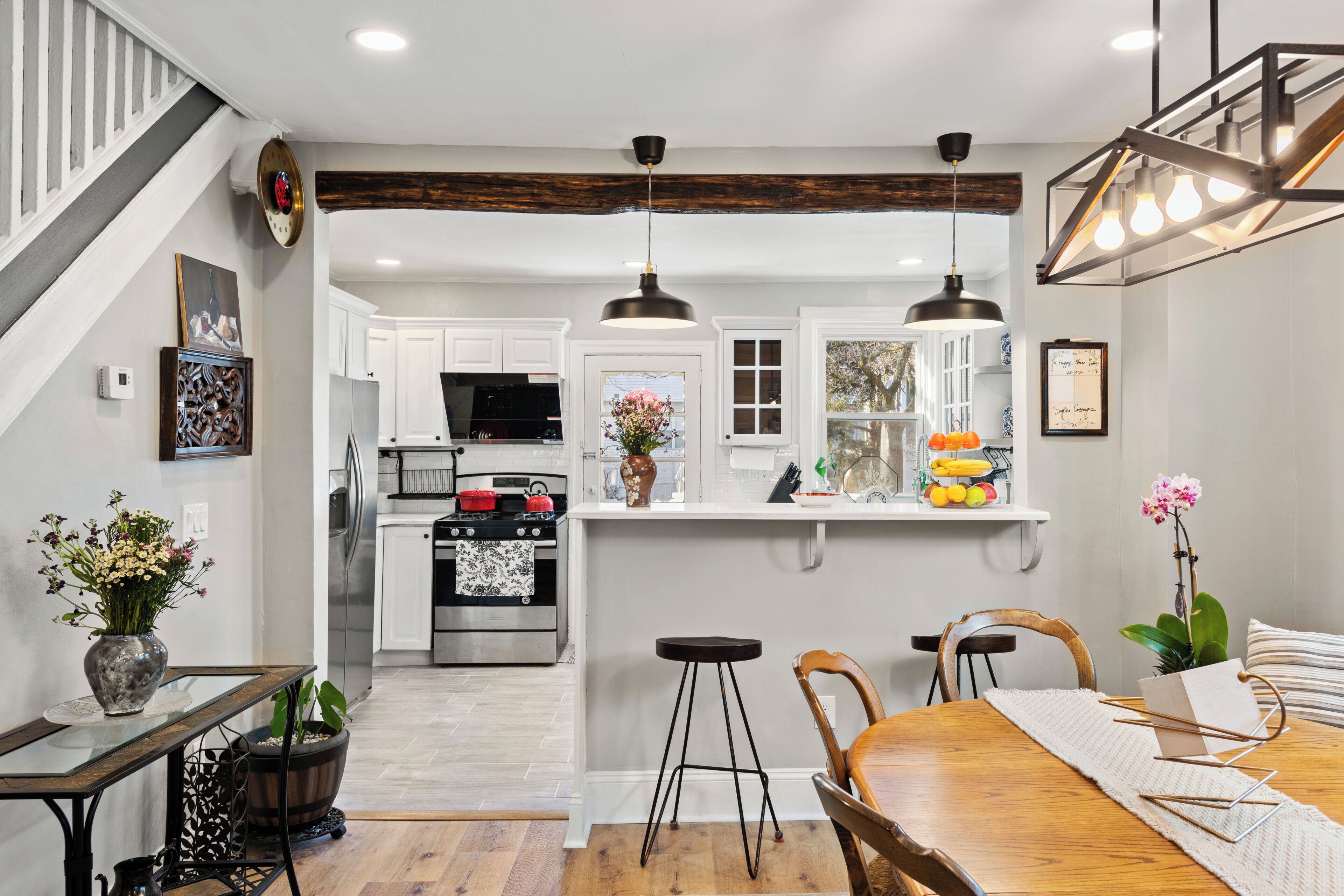 A kitchen with white cabinets, a central island, pendant lighting, and a dining area with a wooden table and chairs.