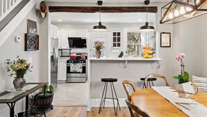 A kitchen with white cabinets, a central island, pendant lighting, and a dining area with a wooden table and chairs. - Sophia's Garden Cottage-  Quality & Stylish & Car-Ps & Walk-Zone & Kid Friendly  (Ardmore)